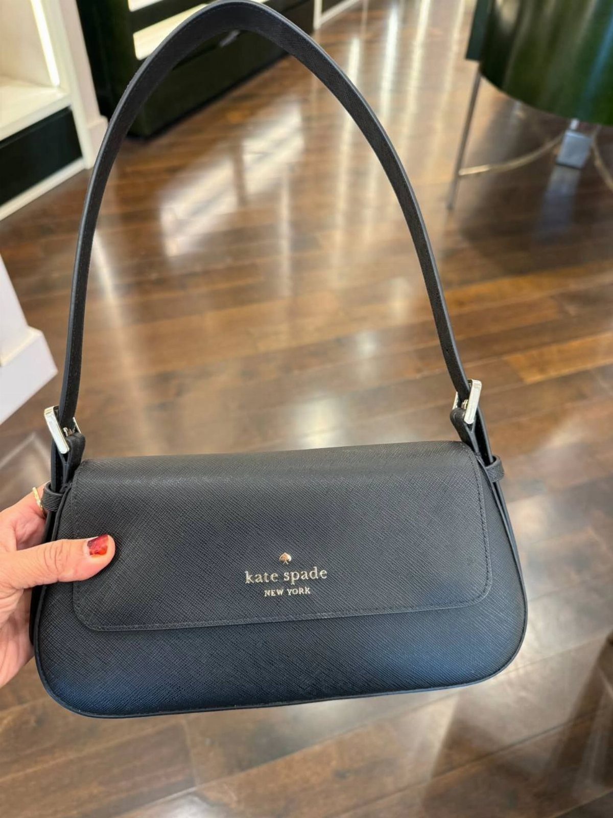 Black Kate Spade shoulder bag with gold lettering held against a wooden floor.