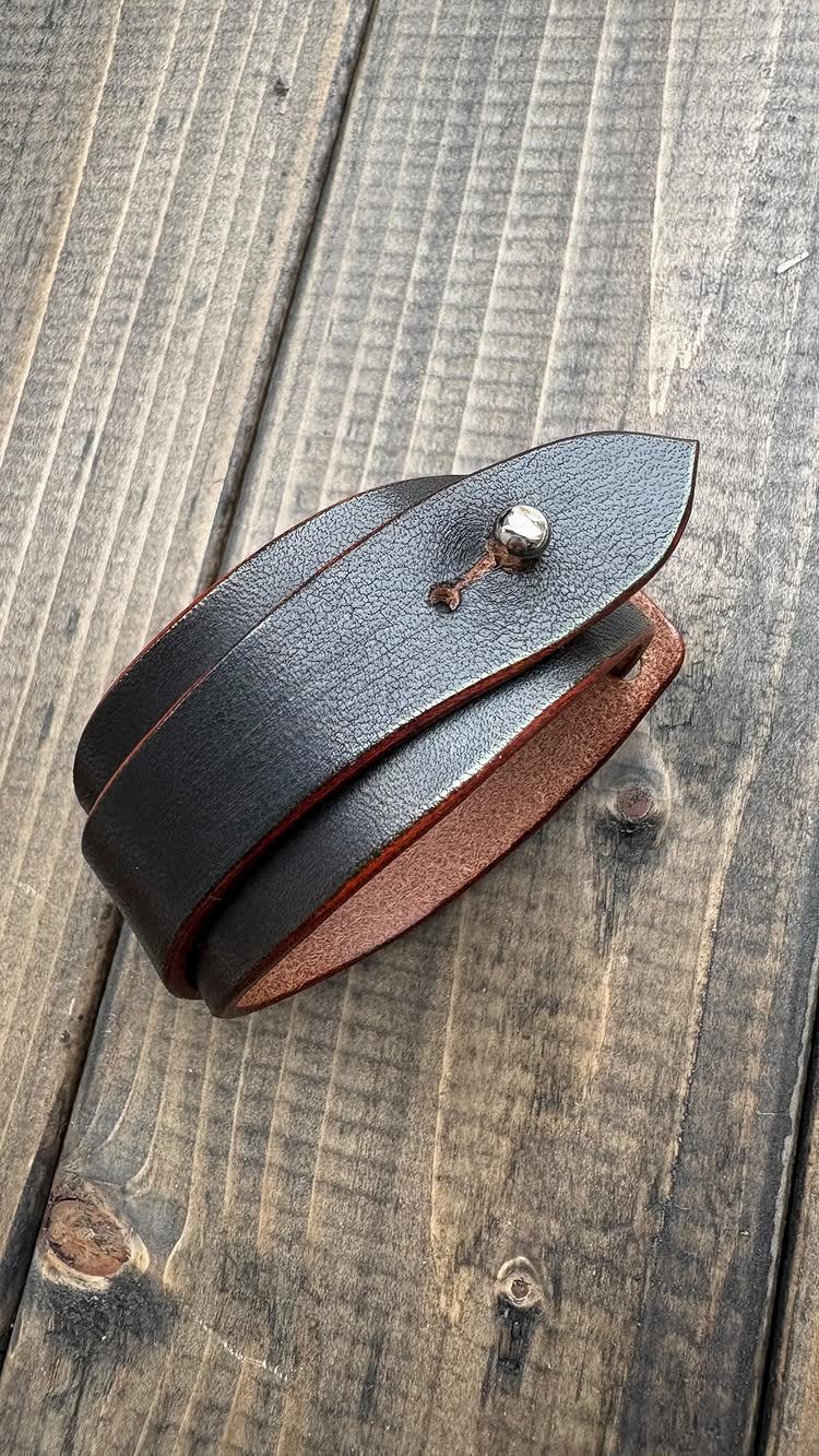 Dark brown leather wrap bracelet with silver stud on a rustic wooden background