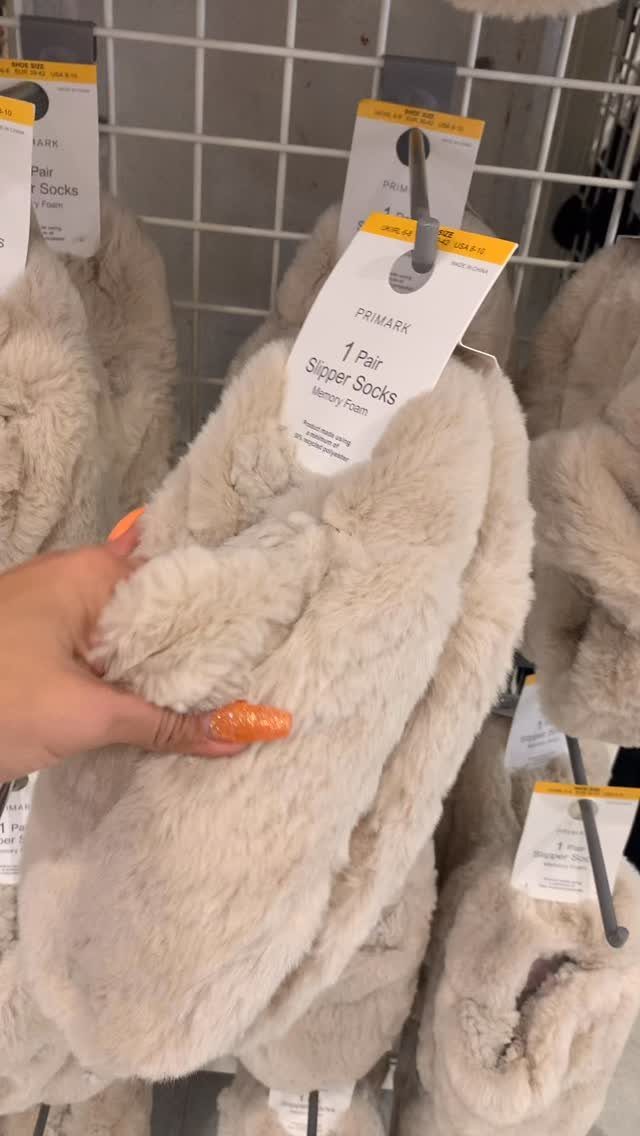 Beige memory foam slipper socks held by a hand in a retail store.