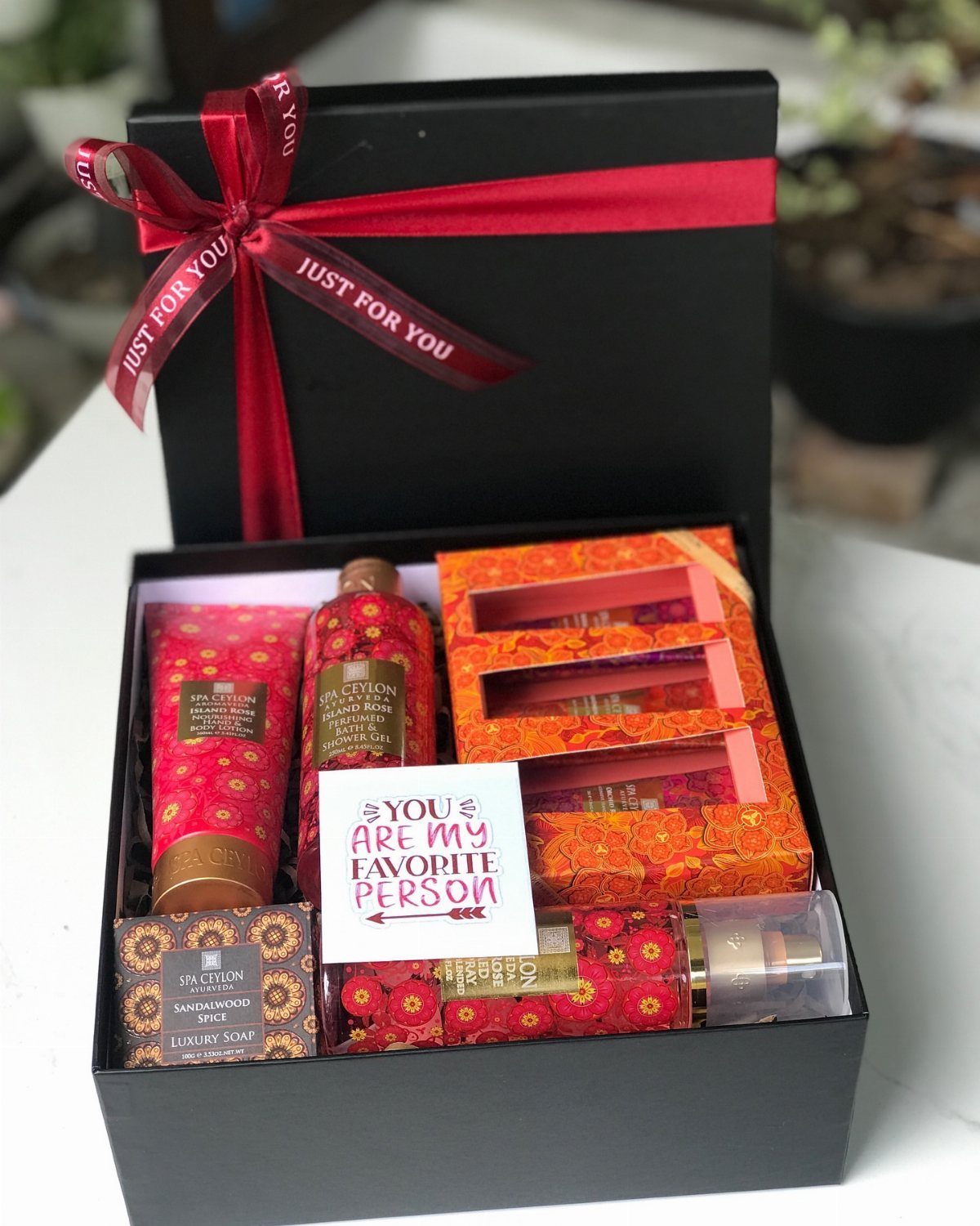 Black gift box with red ribbon containing red patterned bath and body products.