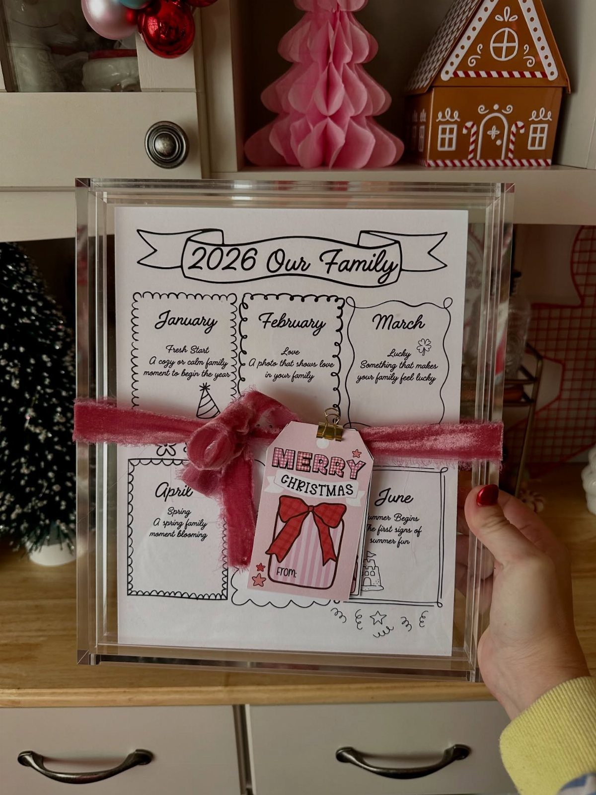 Acrylic frame holding a 2026 family calendar decorated with pink ribbon and tag.