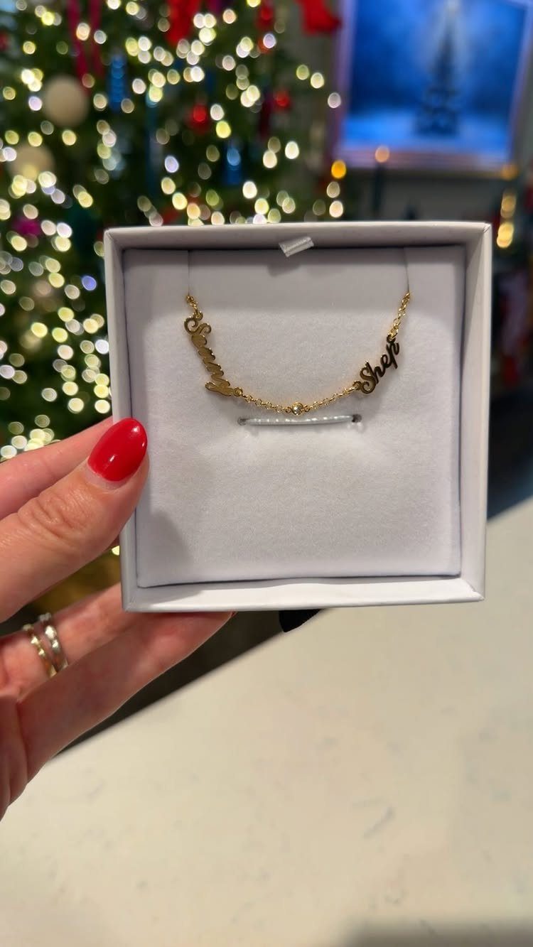 Gold personalized nameplate necklace inside a white jewelry box with Christmas tree background