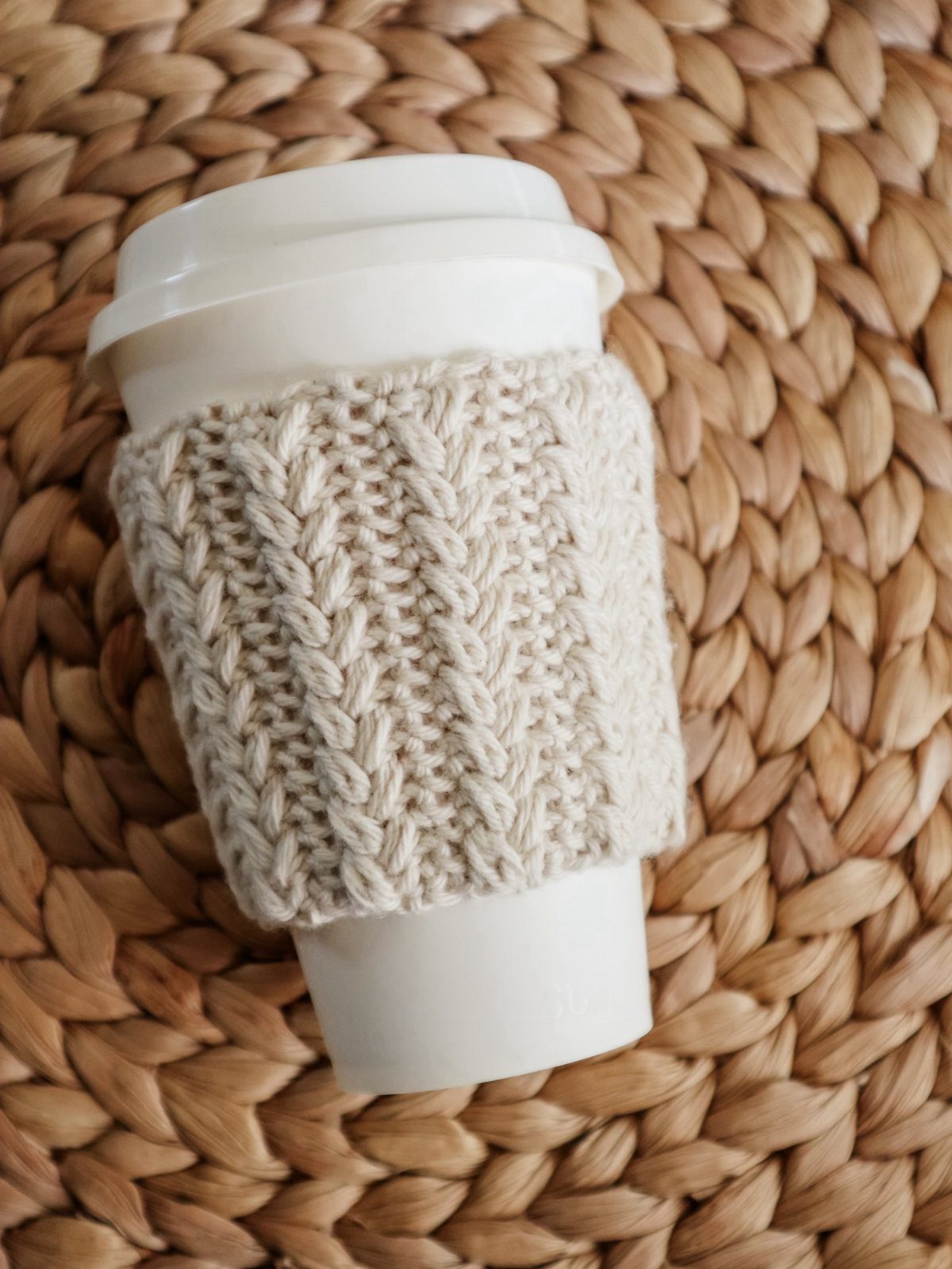 White coffee cup with a cream knitted sleeve on a woven wicker background