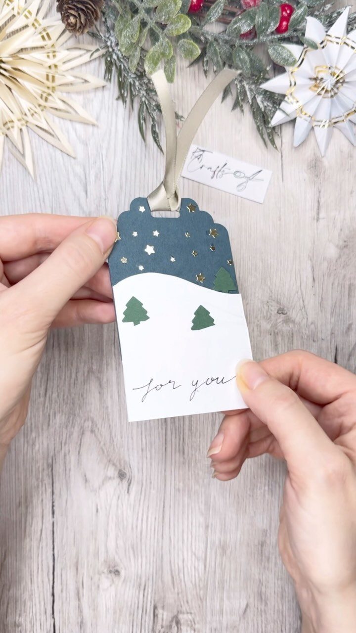 Holiday gift tag with pine trees and stars held by two hands.