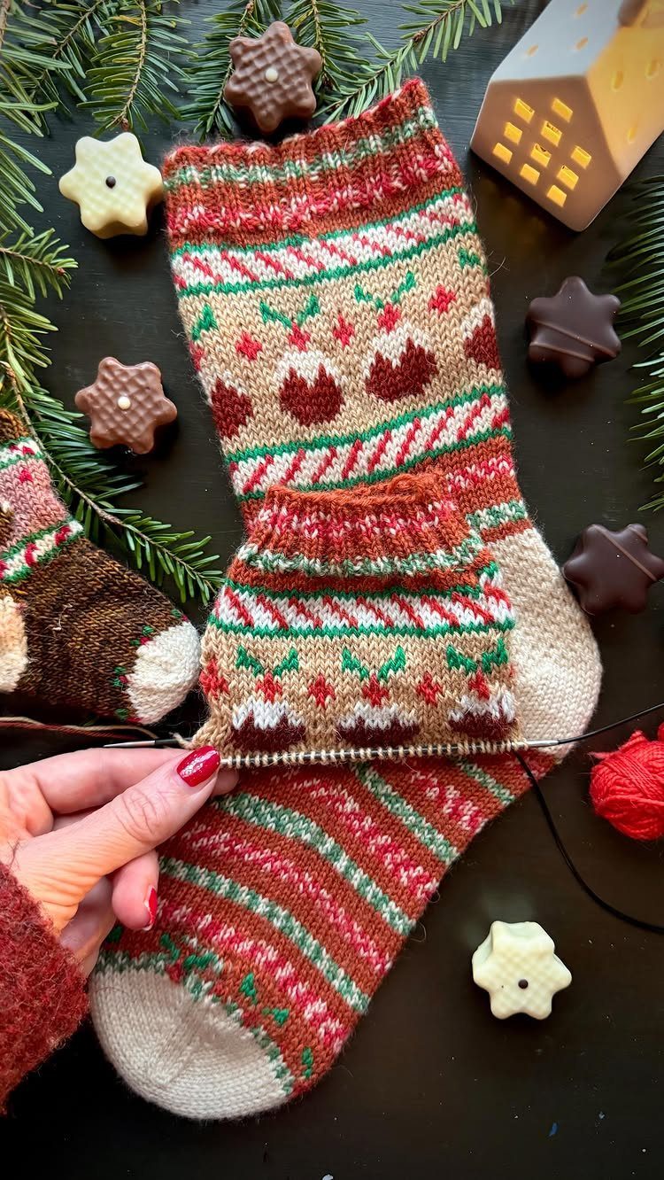 Hand-knitted holiday socks with festive patterns surrounded by star cookies and pine branches.