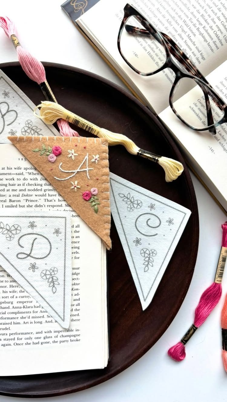 Handmade triangular embroidered bookmarks with letters on a tray next to an open book.