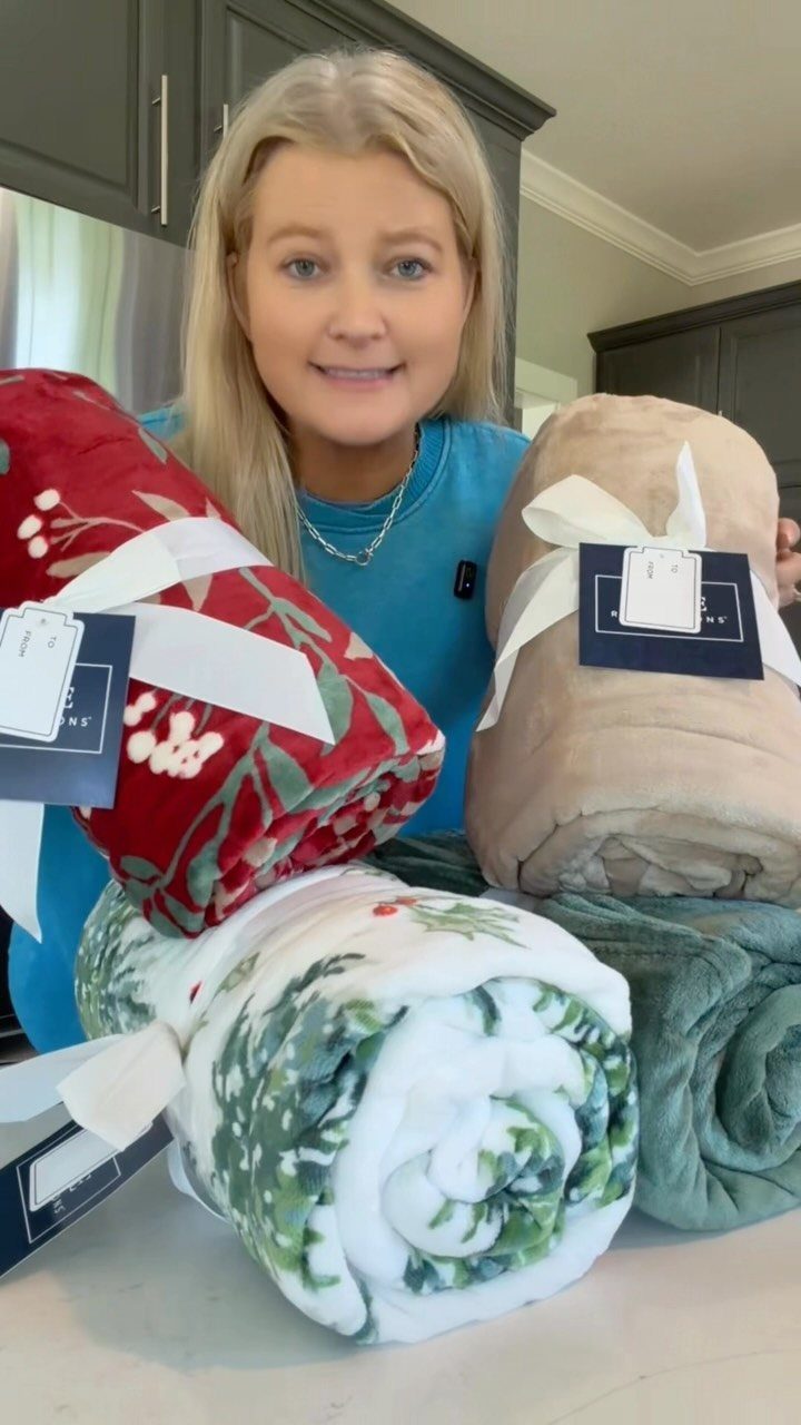 Woman posing with rolled plush blankets tied with ribbons and gift tags.
