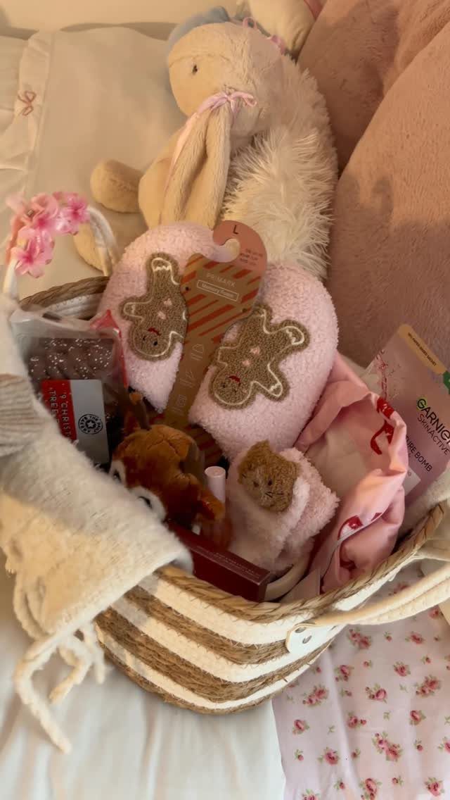 Gift basket with pink gingerbread slippers, plush bunny, and beauty products on floral fabric.