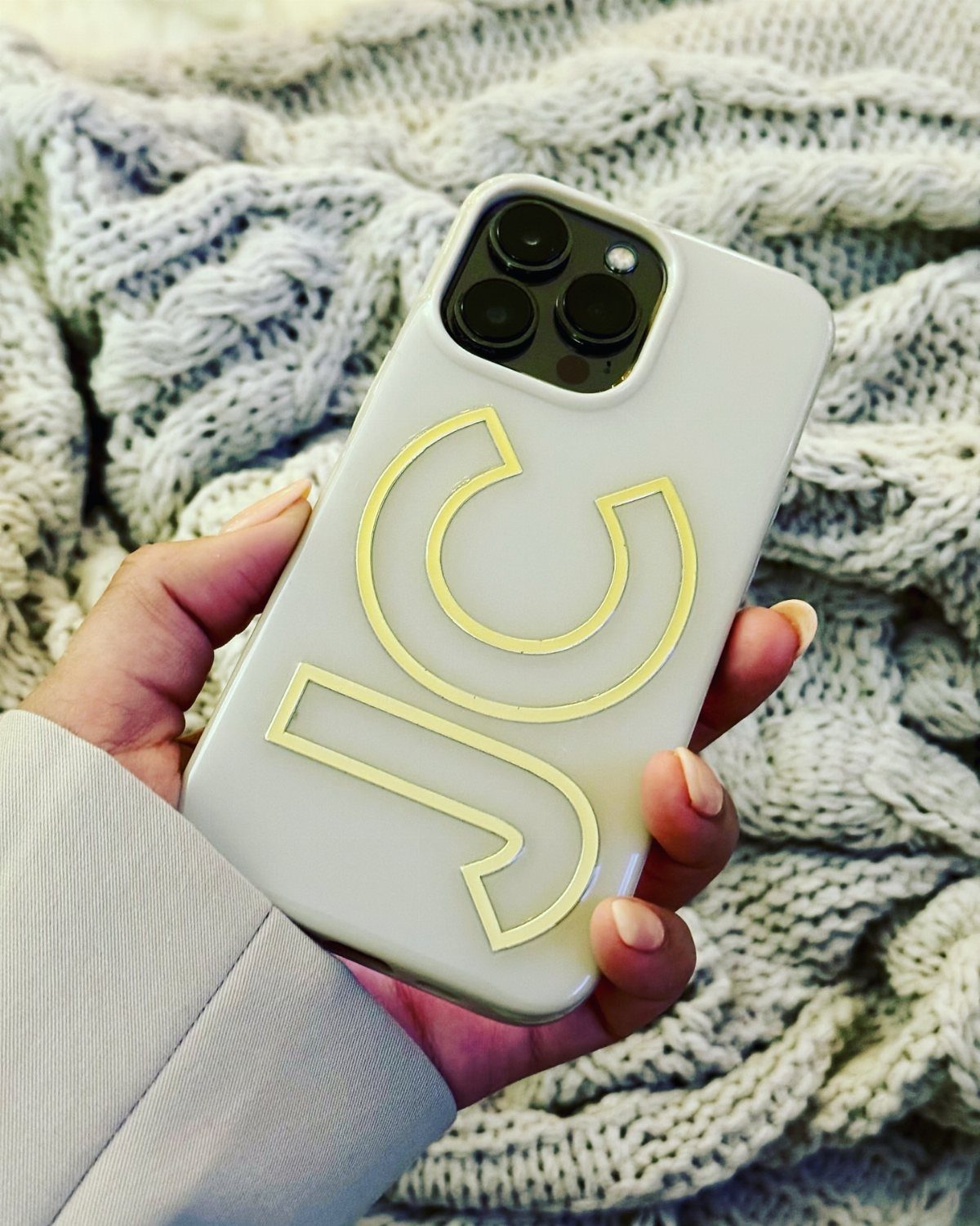 White phone case with yellow JC initials held against a grey knit blanket
