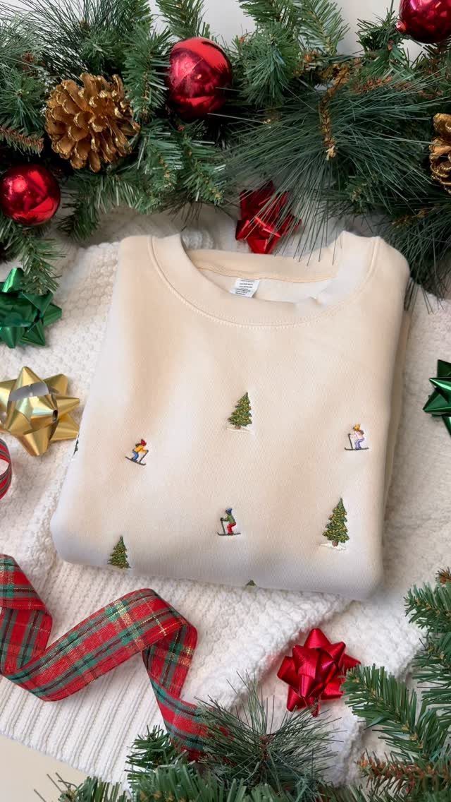 Cream embroidered Christmas sweatshirt on a white knit blanket with festive holiday decorations