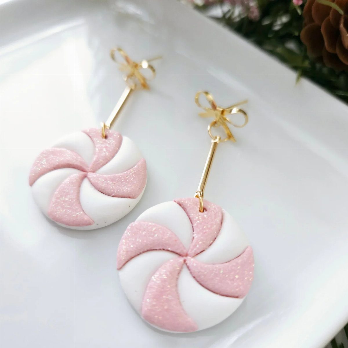 Pink and white peppermint swirl earrings with gold hardware on a white plate