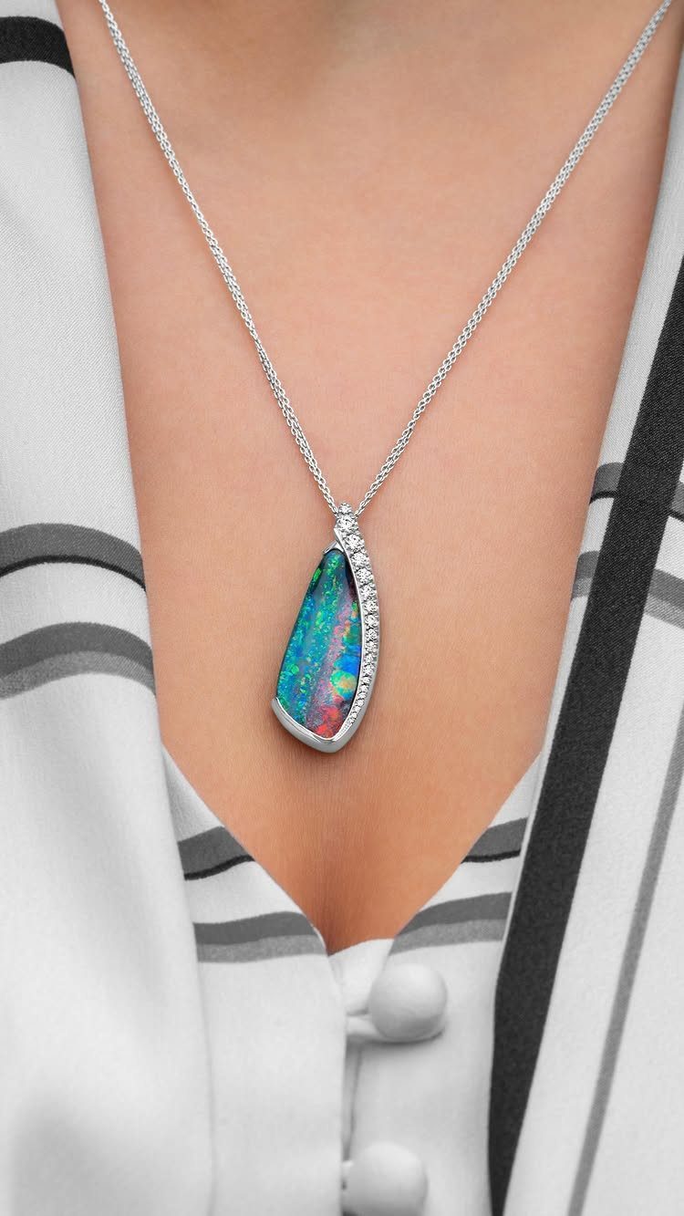 Silver opal pendant necklace worn by a person in a striped white shirt