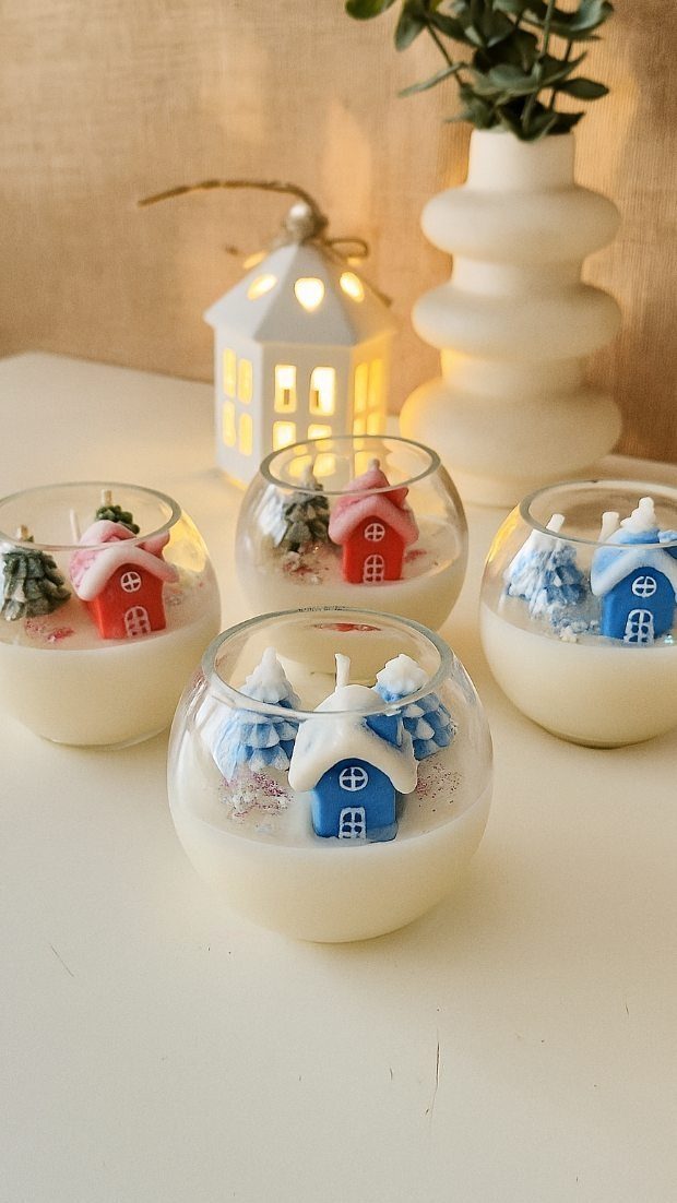 Four glass bowl candles featuring miniature wax houses and trees in white wax.
