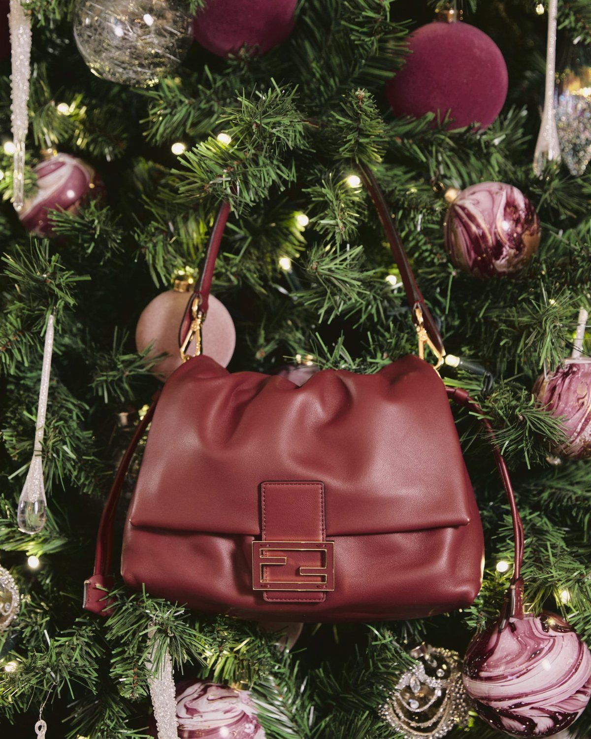 Red leather handbag with gold clasp hanging on a decorated Christmas tree