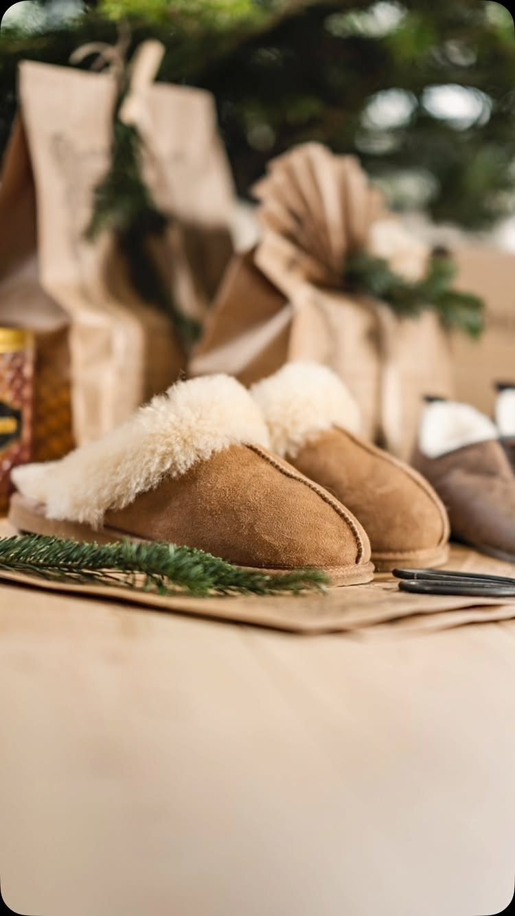 Brown suede slippers with white faux-fur lining next to wrapped Christmas gifts.