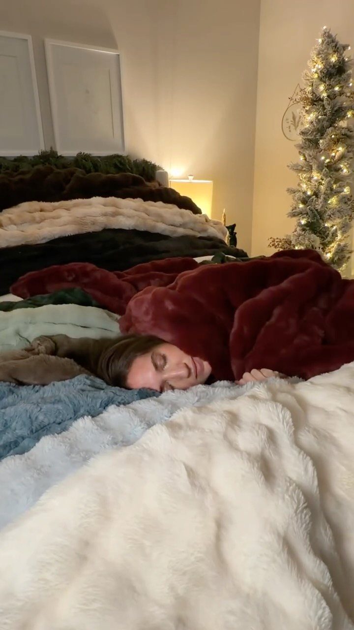Woman sleeping under a stack of colorful, plush faux fur blankets near a Christmas tree