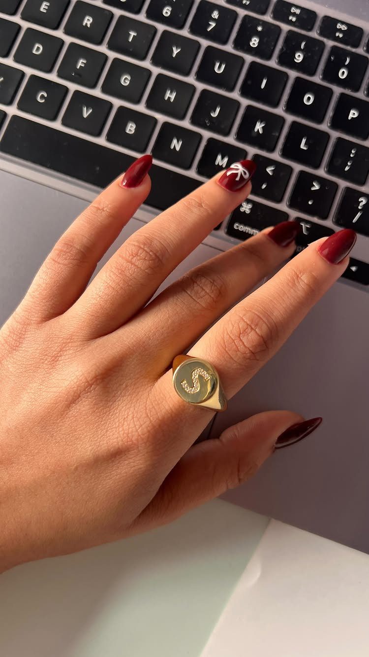 Gold signet ring with letter S on a hand with red nails