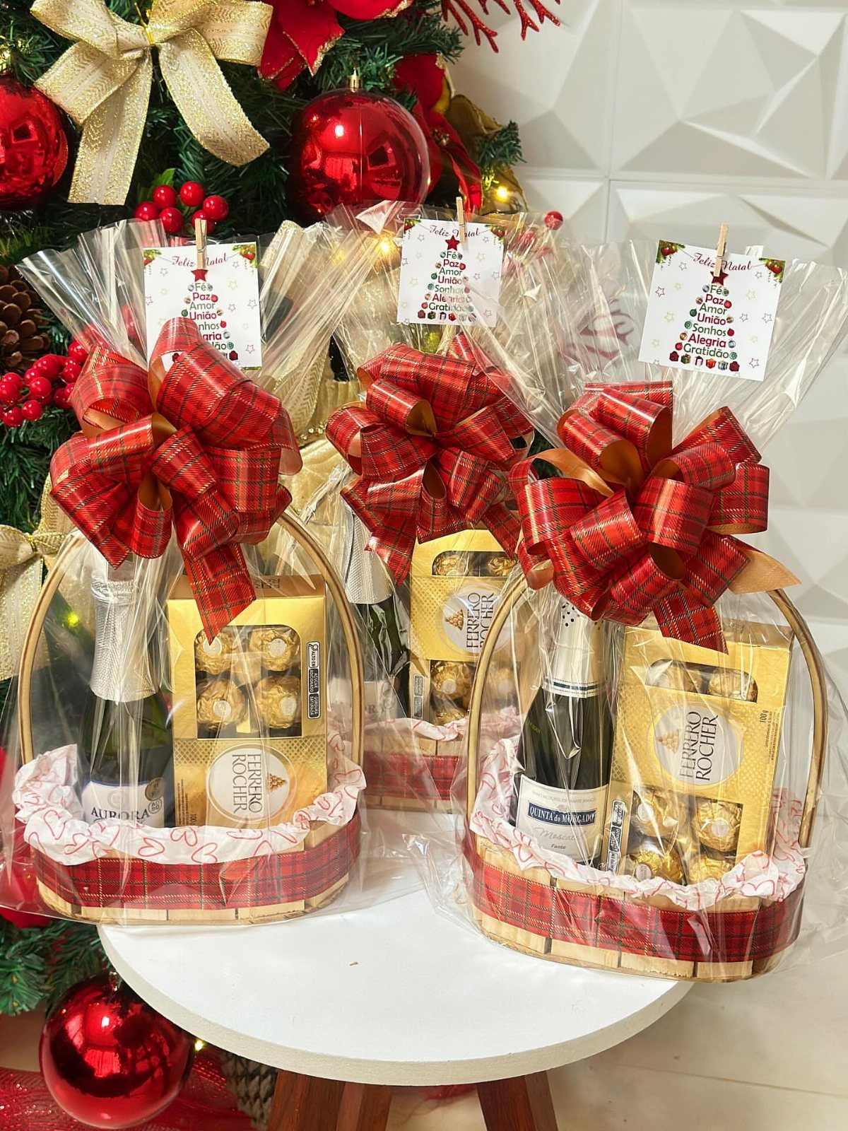 Three Christmas gift baskets with wine and chocolates wrapped in red gold bows.