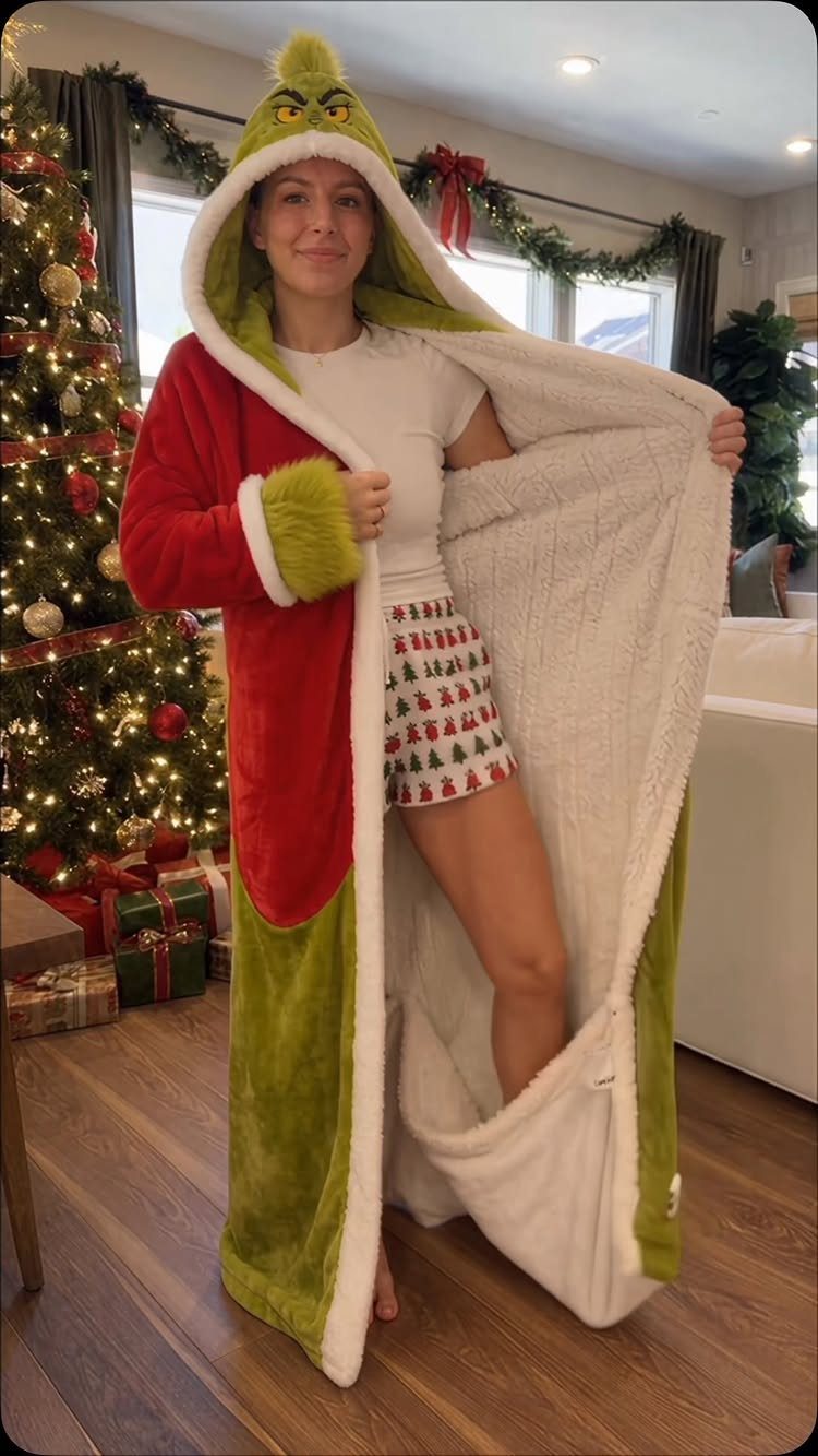 Woman wearing a Grinch hooded robe standing next to a decorated Christmas tree.
