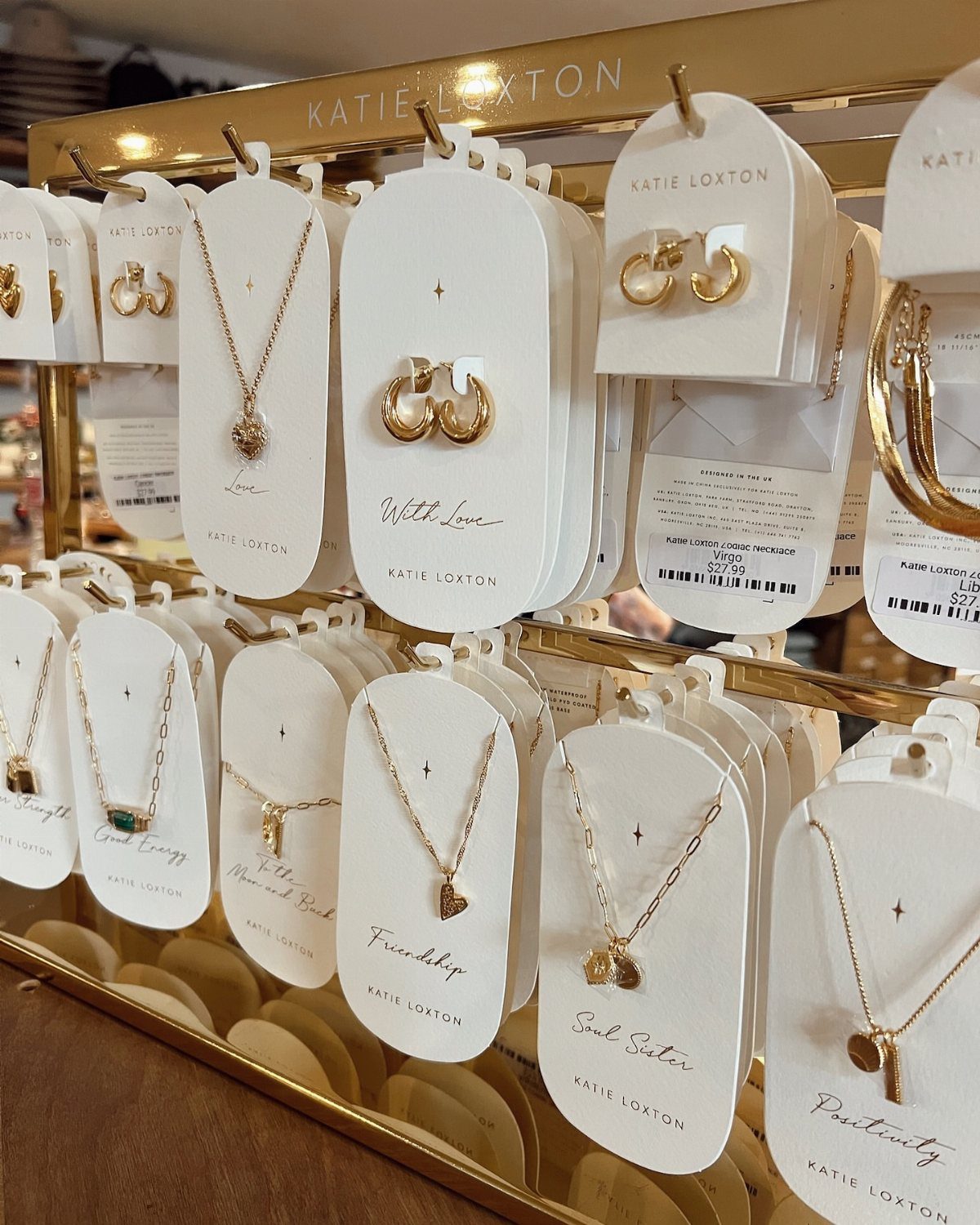 Gold necklaces and earrings on white display cards on a gold store rack.