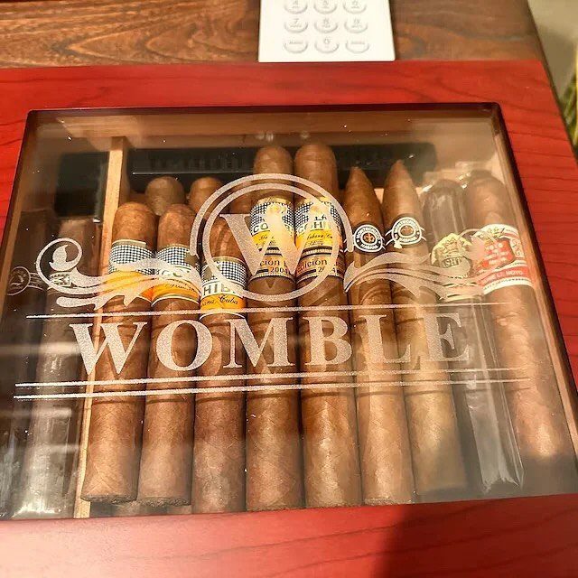 Assorted brown cigars in a clear acrylic box with Womble etched on front