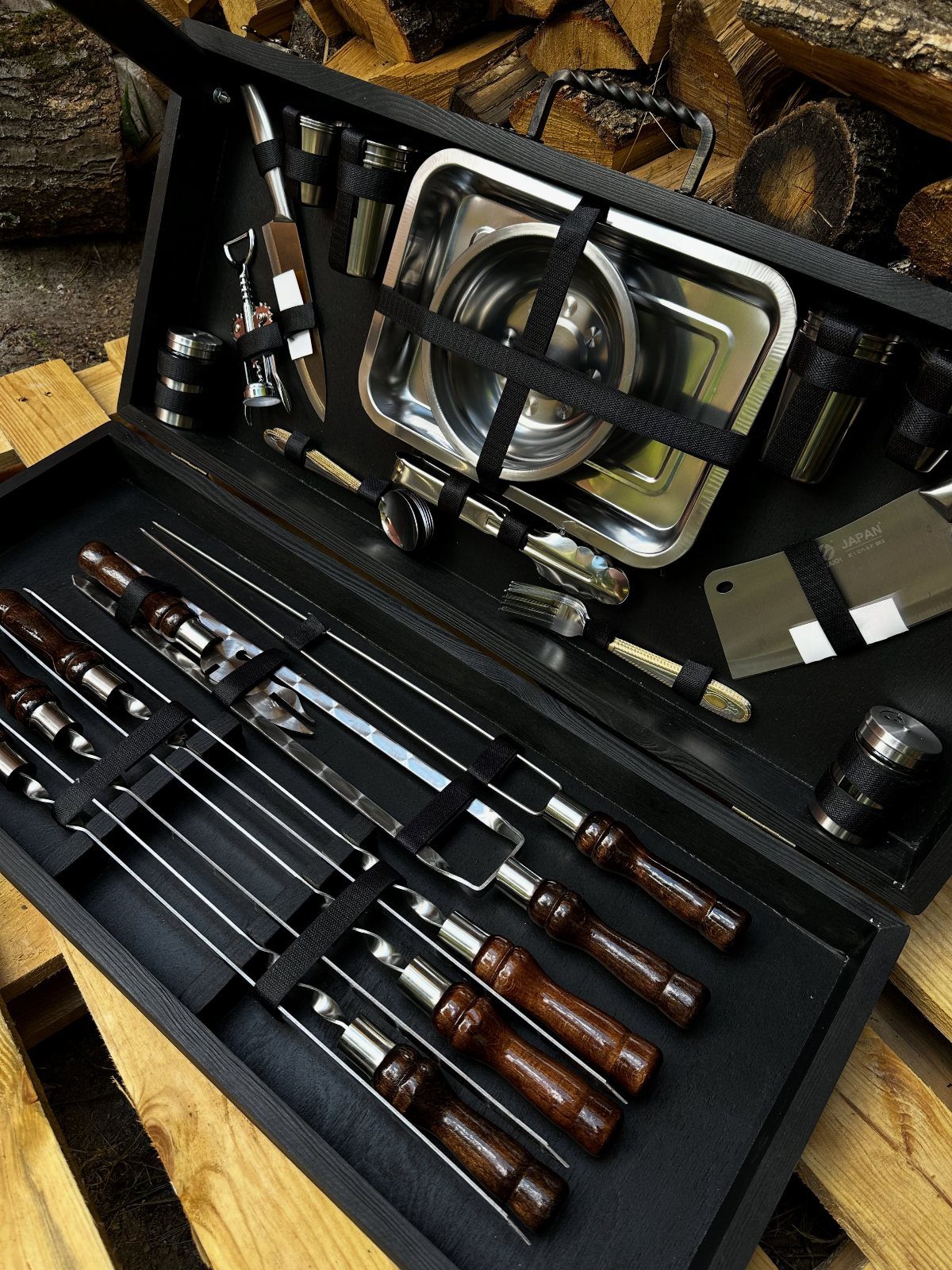 BBQ tool set with wooden handles in a black case near firewood logs