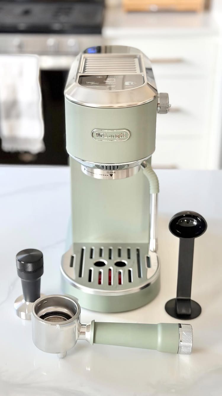 Light green espresso machine with portafilter and tamper on a white kitchen counter