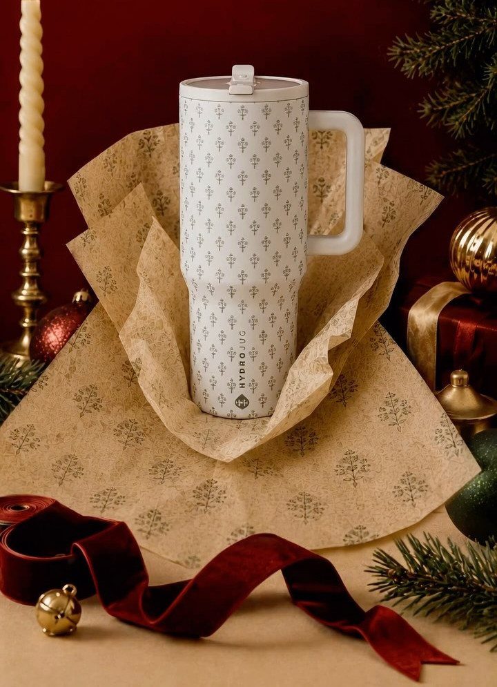 White patterned travel mug wrapped in gold tissue paper with Christmas decorations.