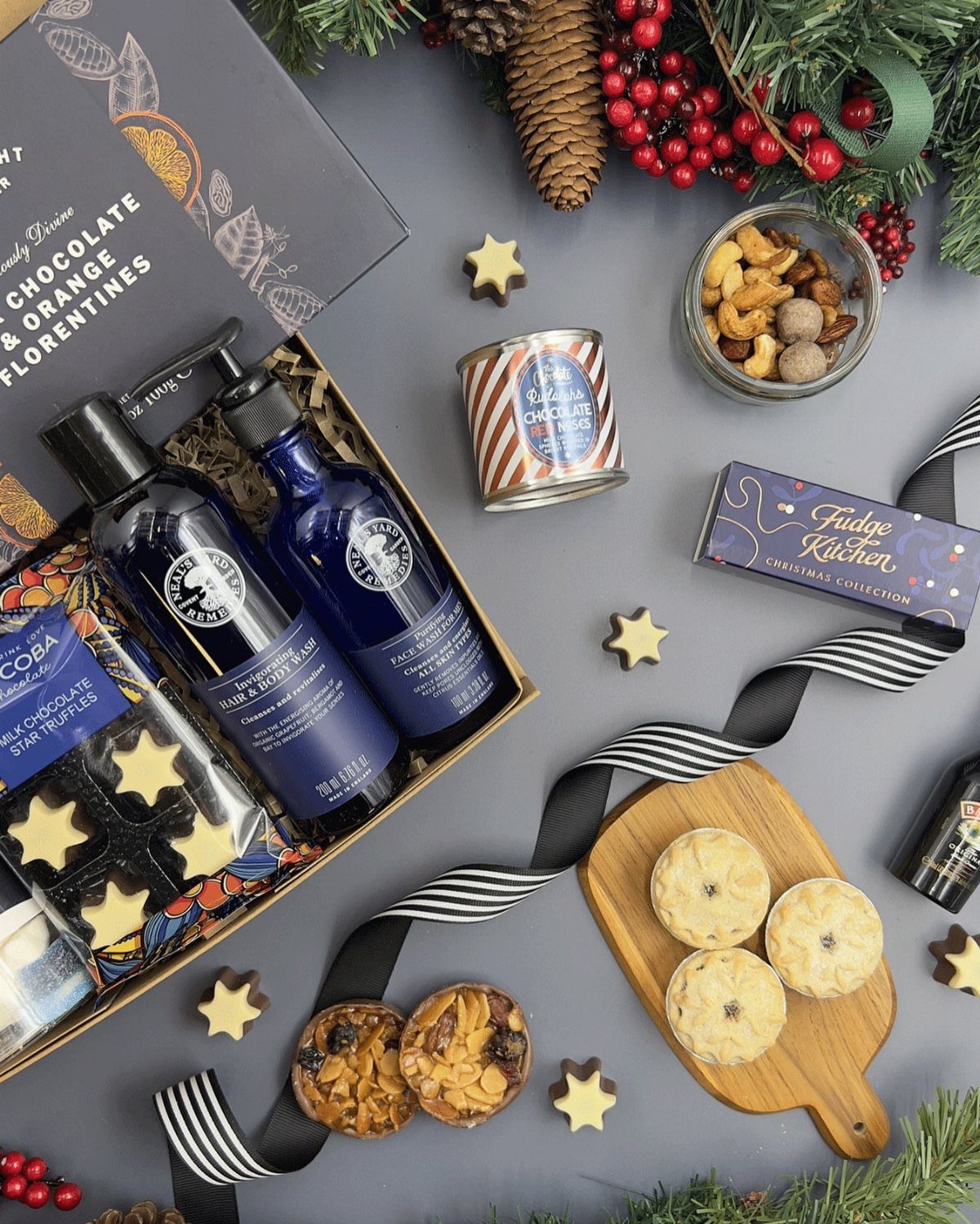 Christmas gift hamper with toiletries, chocolates, and treats surrounded by festive holiday decorations.
