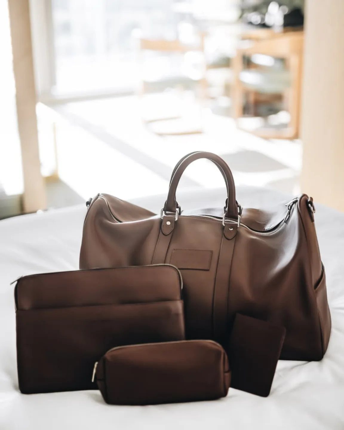Brown leather duffle bag with matching travel pouches on a white surface.