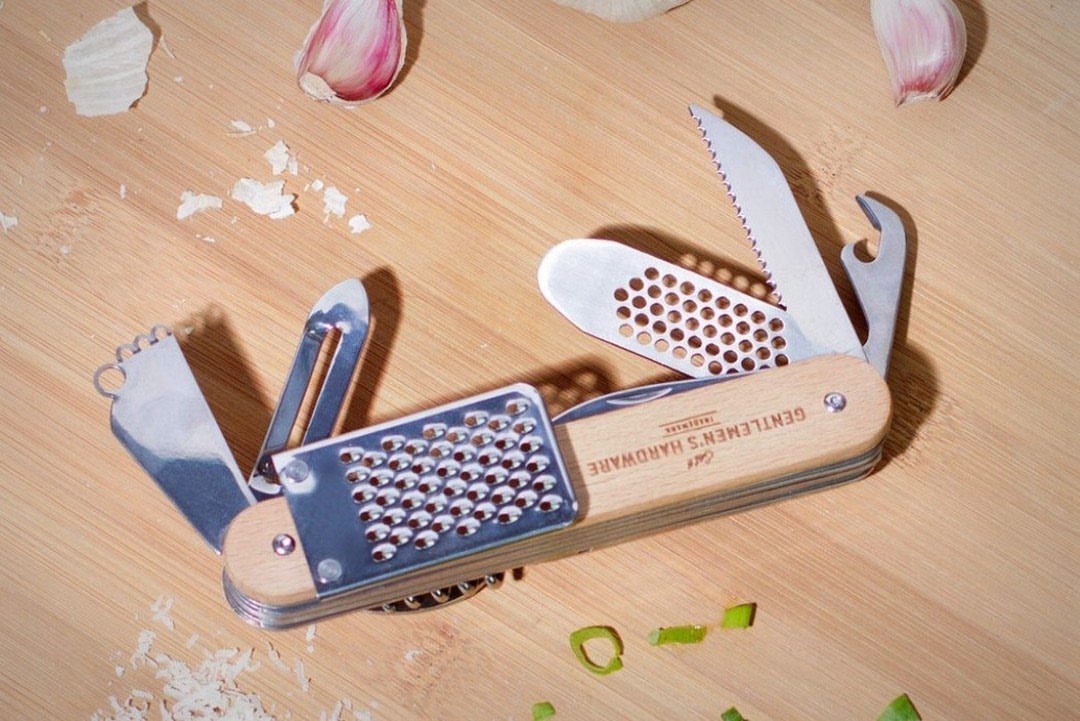 Multi-tool pocket knife with unfolded attachments on a wooden board with garlic cloves.