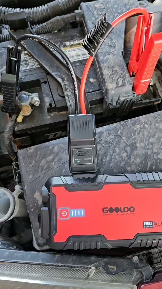 Portable red jump starter battery connected to a car battery in engine bay