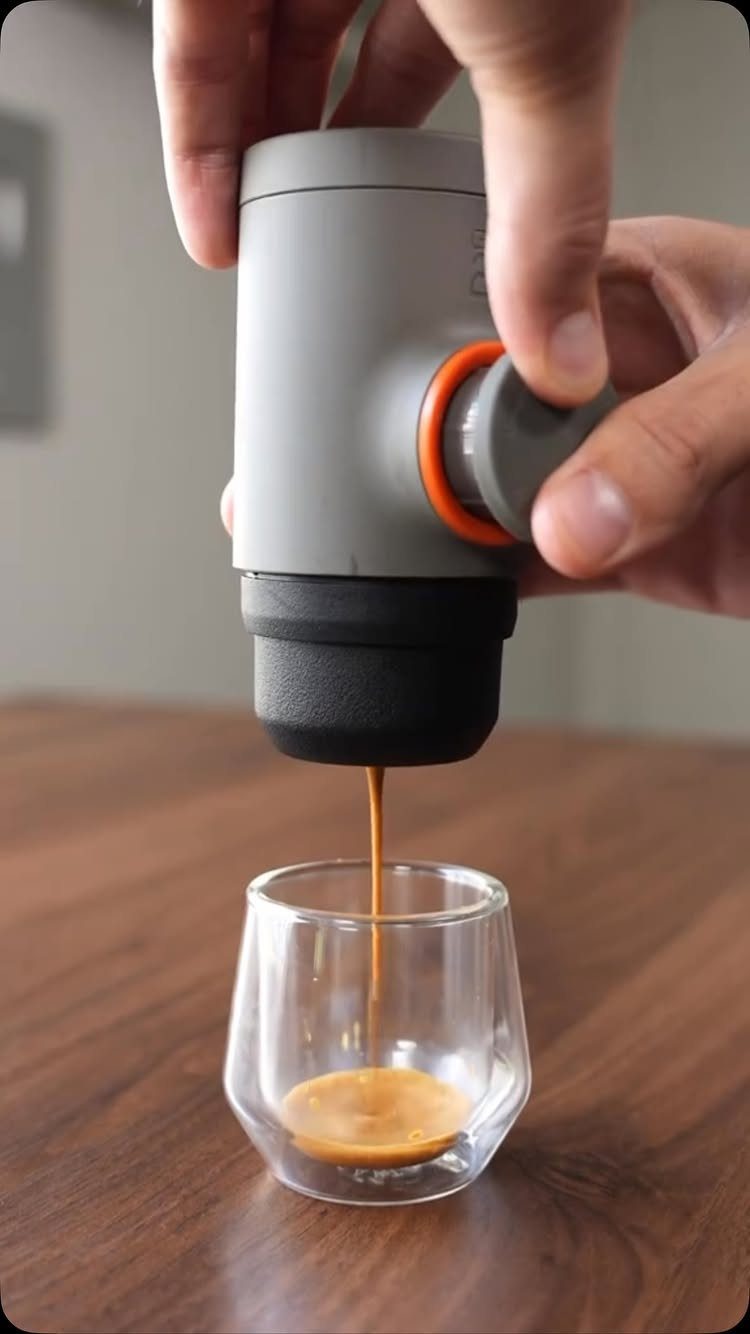 Portable espresso maker pouring coffee into a small clear glass on wooden table