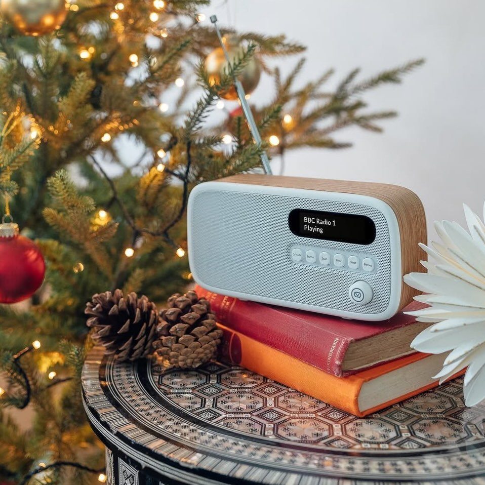 Digital radio with wood accents on books next to a decorated Christmas tree
