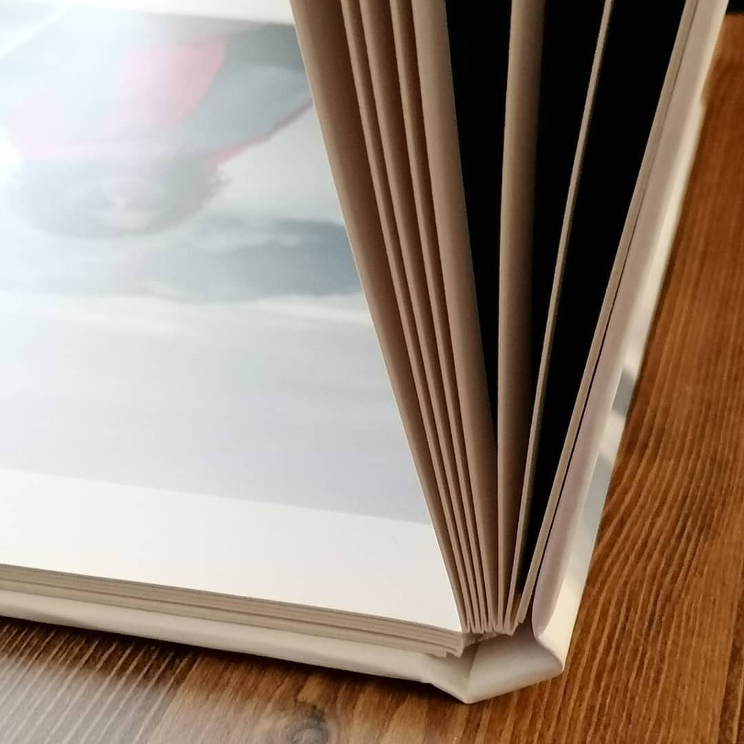 Open photo album with thick white pages resting on a wooden table surface.