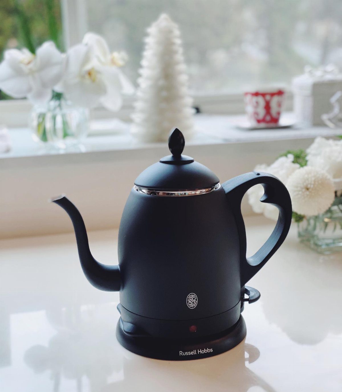 Matte black electric gooseneck kettle on a white counter with festive winter decorations.