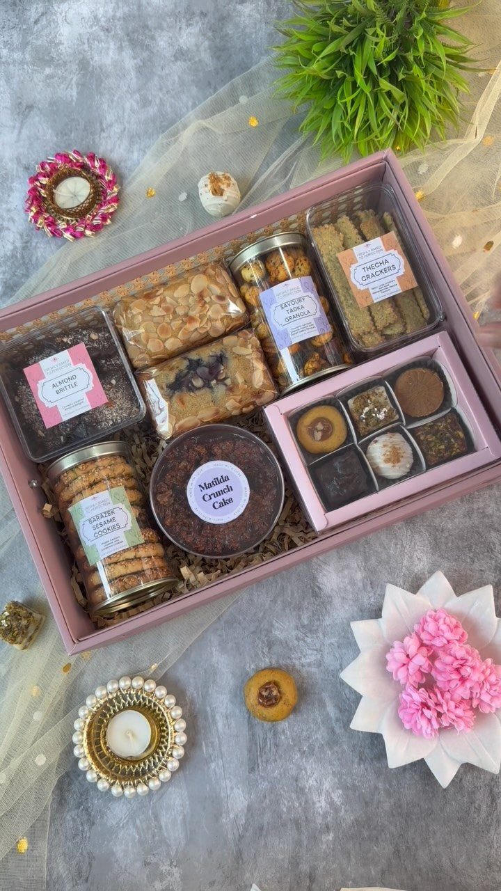 Pink gift box filled with gourmet cookies, sweets, and spices on grey background.