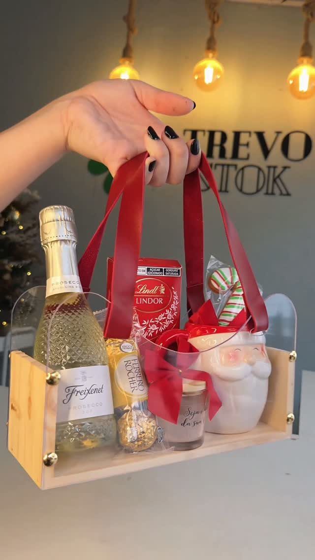 Wooden gift tray with sparkling wine, chocolates, and a mug held by a hand