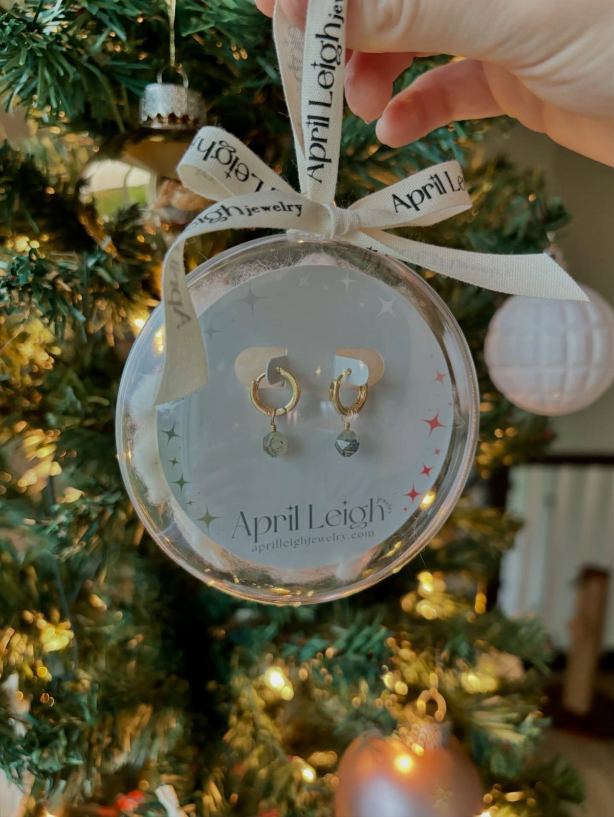 Gold hoop earrings in a clear ornament hanging on a decorated Christmas tree