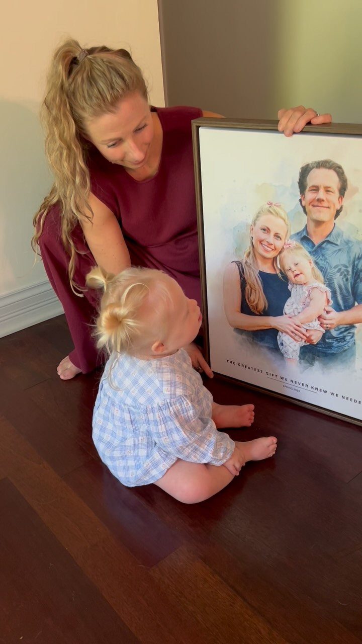 Woman and toddler looking at a framed custom family portrait illustration on the floor