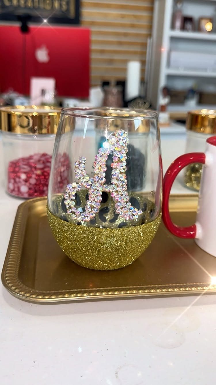 Stemless wine glass with gold glitter base and rhinestone letter A on gold tray