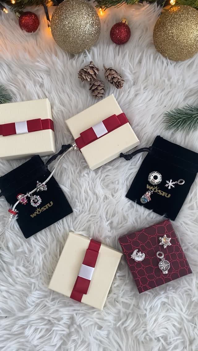 Silver charm bracelet and gift boxes on white faux-fur with Christmas ornaments.