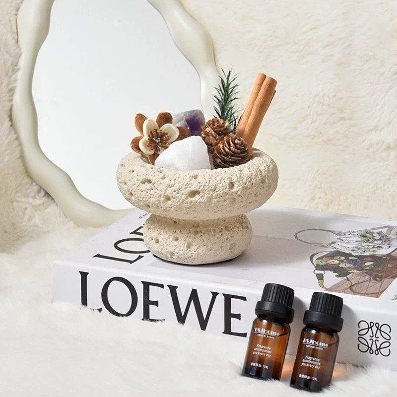 Stone aromatherapy dish with crystals and cinnamon sticks next to essential oil bottles.