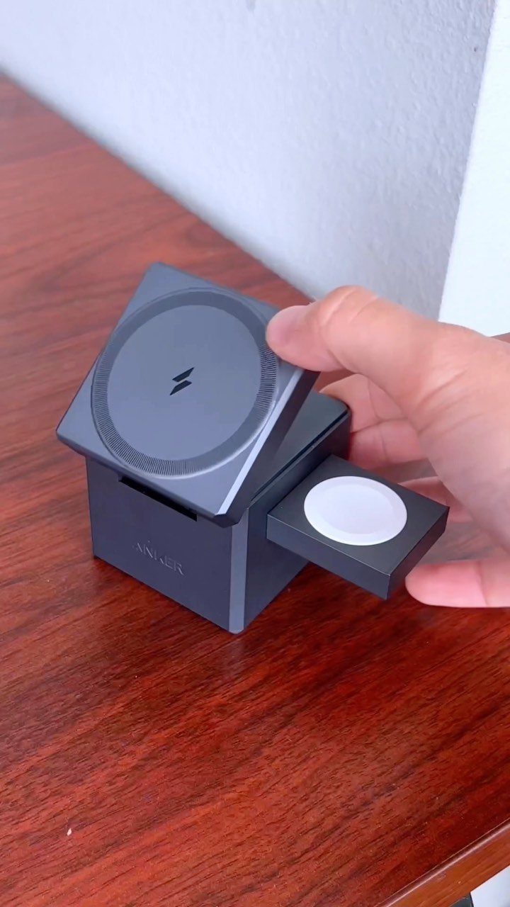 Black electronic charging station with a circular pad and sliding drawer on wood.