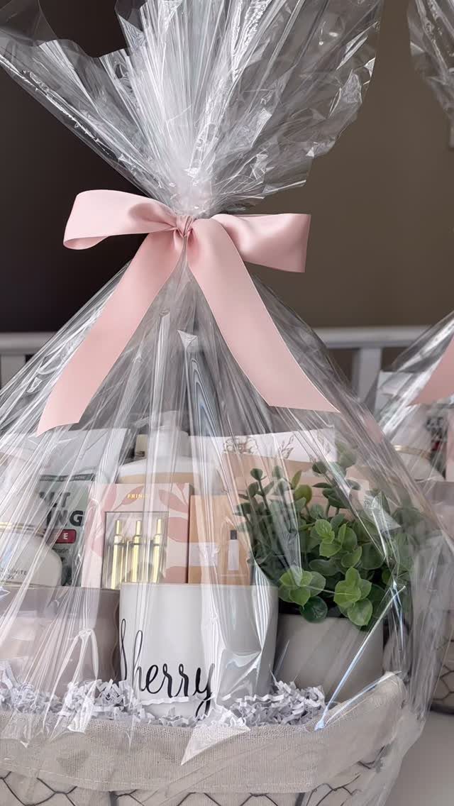 Gift basket wrapped in cellophane with a pink bow containing a mug and plant