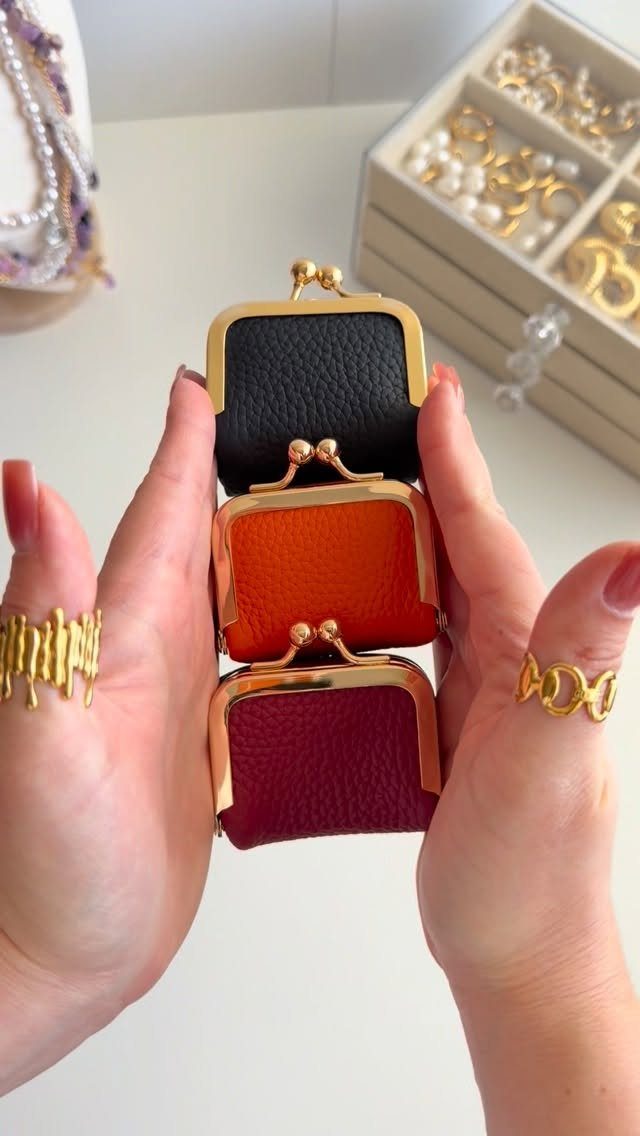 Three small leather coin purses in black, orange, and burgundy held by hands.