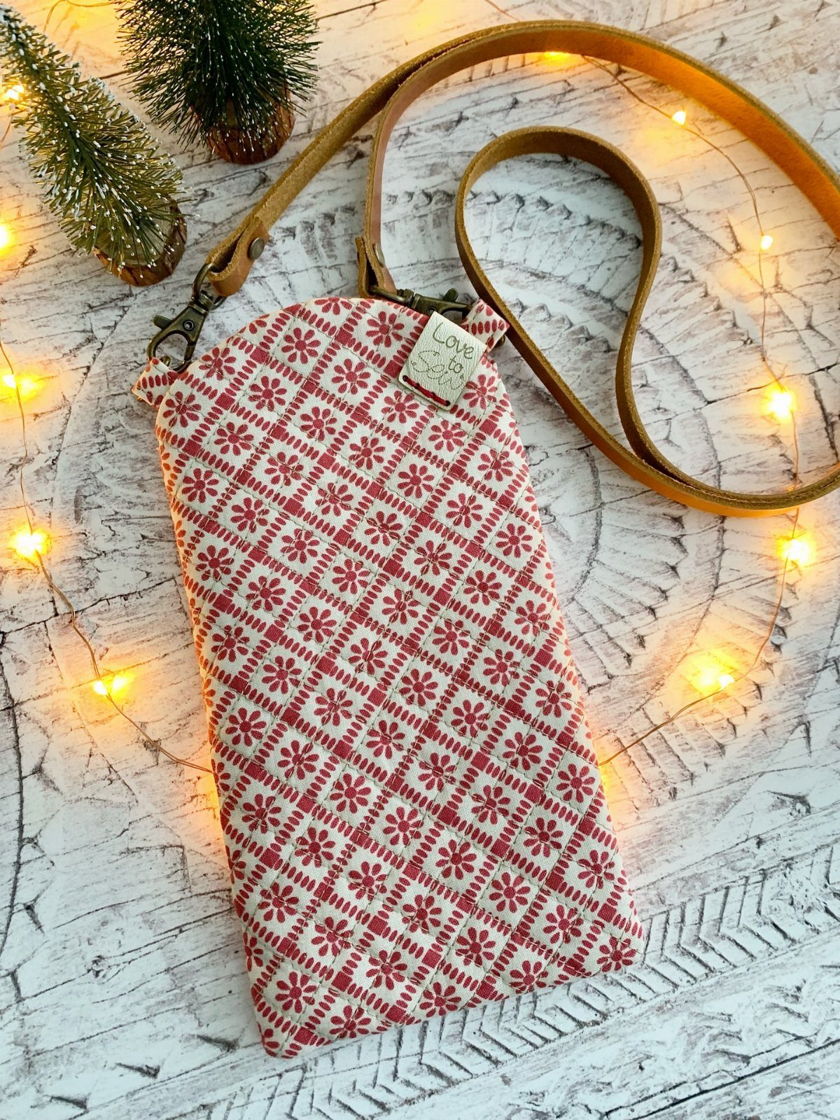 Red and white patterned slim crossbody pouch with leather strap on wooden background.