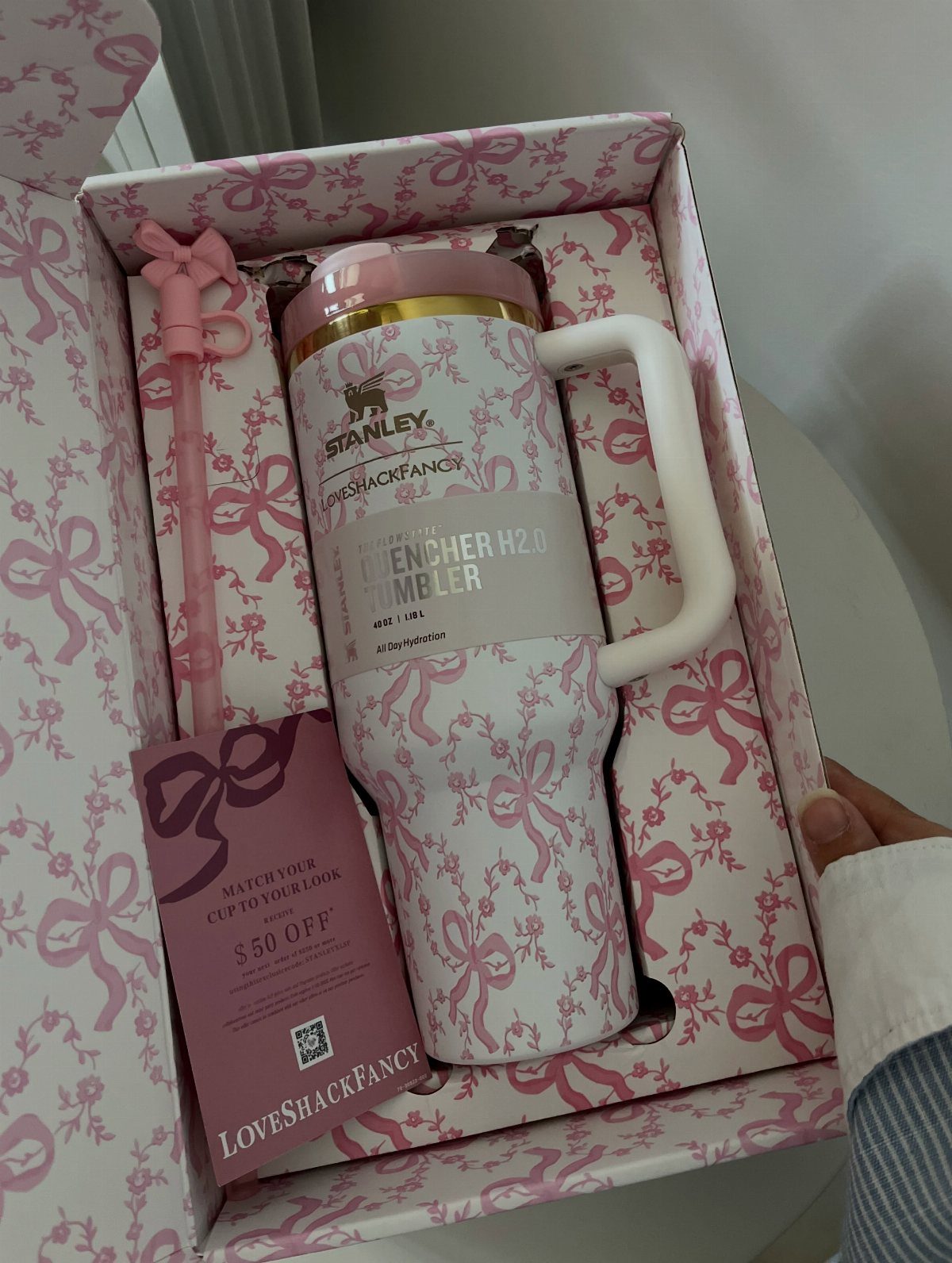 White Stanley Quencher tumbler with pink bow patterns inside a matching gift box.