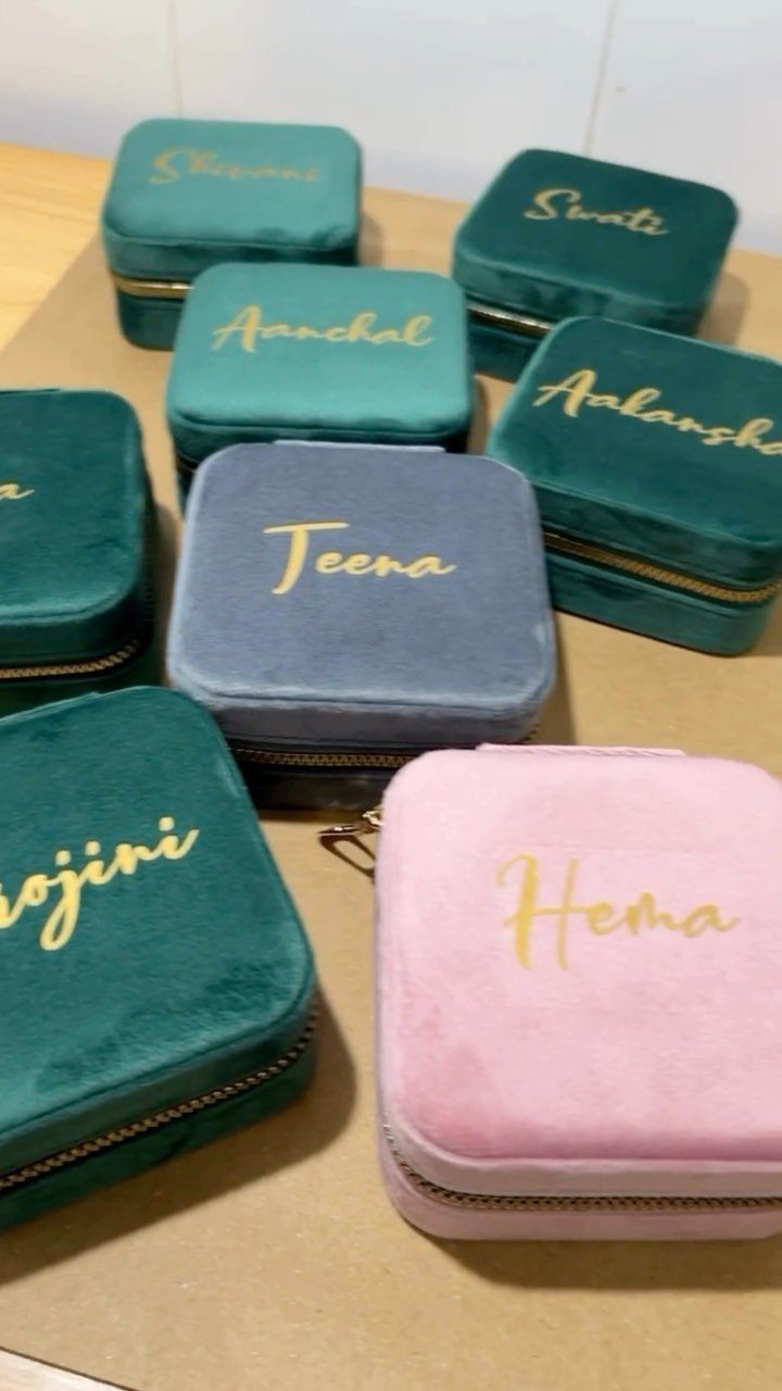 Velvet travel jewelry cases in green, pink, and grey with personalized gold names.