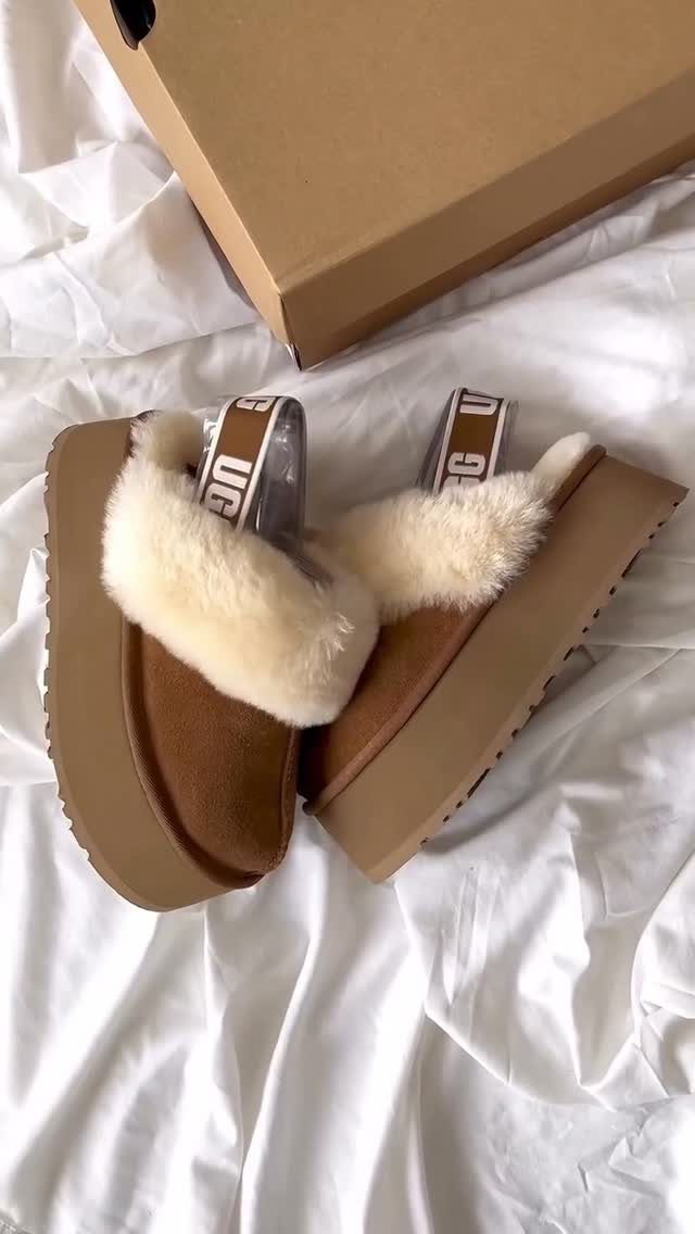 Brown platform Ugg slippers with white fur lining on white wrinkled fabric.